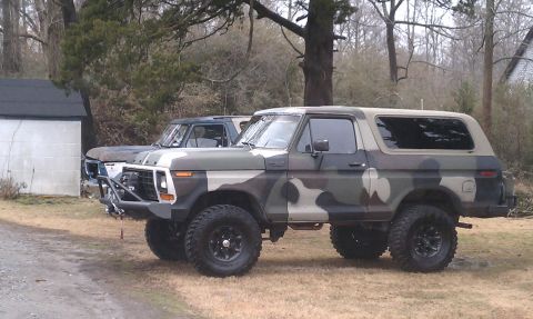 1979 Ford Bronco - A lifted, camouflage-painted 1979 Ford Bronco is parked next to another vehicle.
