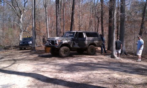 1979 Ford Bronco - A camouflaged Ford Bronco is parked in a wooded area, with another vehicle in the background.