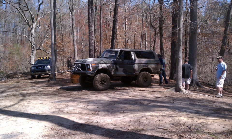 Camouflaged Ford Bronco with off-road tires and bumper, another SUV is visible in the background being winched