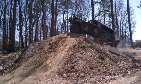 1979 Ford Bronco - A vehicle navigates an obstacle on a dirt track surrounded by trees.