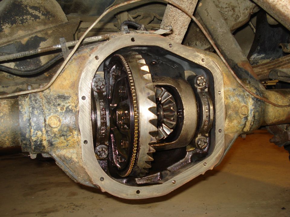 Open differential housing with gears visible. Rusty axle tubes and leaf springs in background