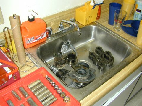1996 Ford Bronco - Various automotive components, including chains and gears, are soaking in a sink next to a toolbox and cleaning supplies.