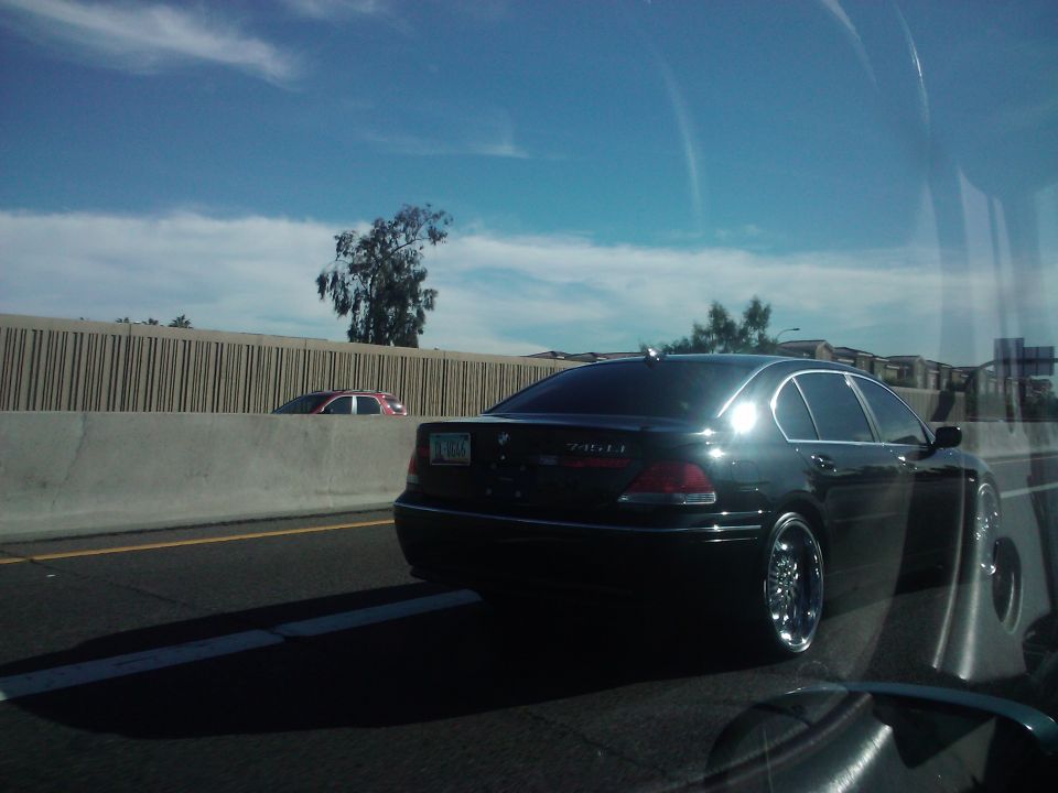 Black BMW 740iL on highway, seen from behind. Another car is visible in the distance