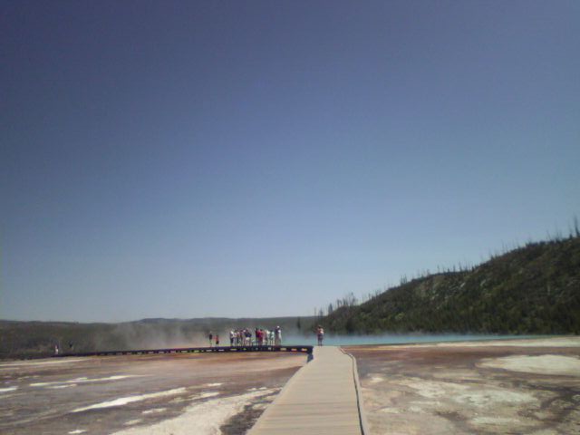 Wooden boardwalk through a geothermal area with a blue sky