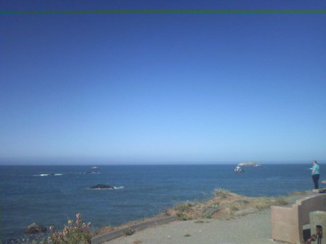 Ocean view with rocks and a distant boat, a person stands on a concrete structure