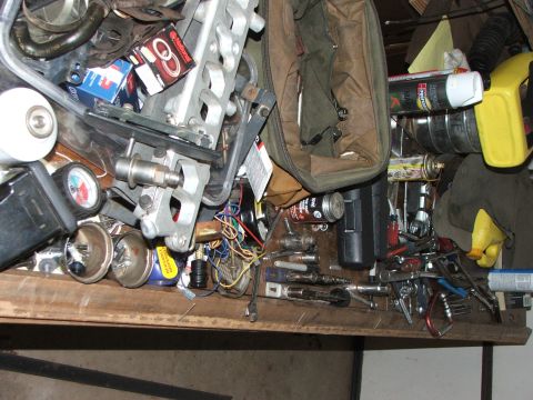 1965 Ford Mustang - A disorganized workbench displays a variety of tools, engine components, and gauges, suggesting a busy automotive workspace.