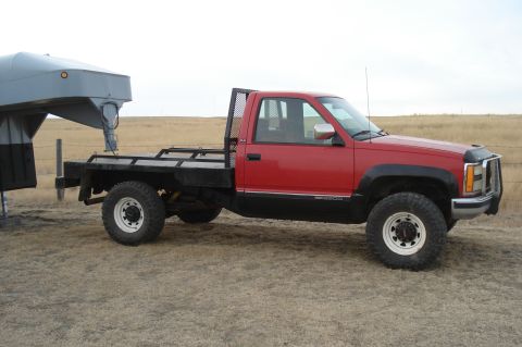 1994 GMC Sierra 3500 - A red GMC pickup truck with a flatbed and gooseneck hitch is parked on a dry, grassy field.