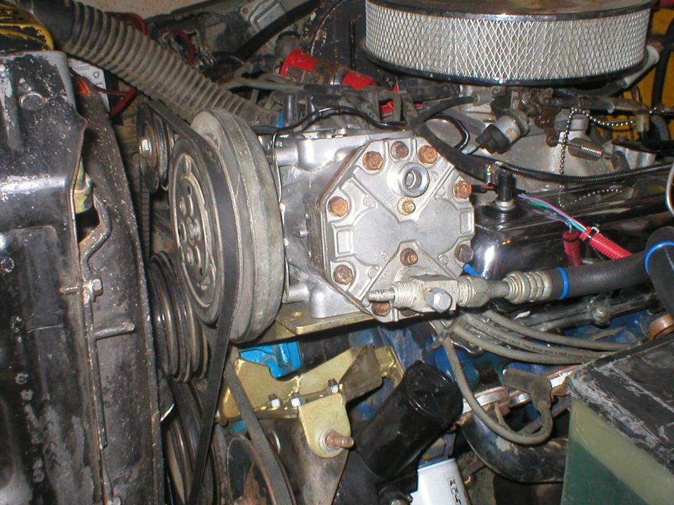 Close-up of an engine bay showing an air conditioning compressor, belts, and pulleys