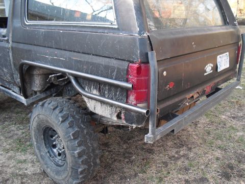 1986 Ford Bronco - Rear view of a black SUV with aftermarket roll cage and bumper, showing off its modifications.