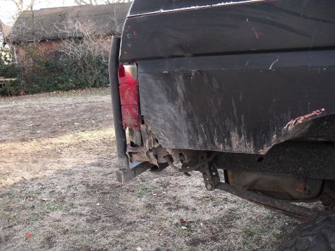 1986 Ford Bronco - The rear of a black SUV shows significant rust and damage, with a spare tire mount and leaf spring visible.