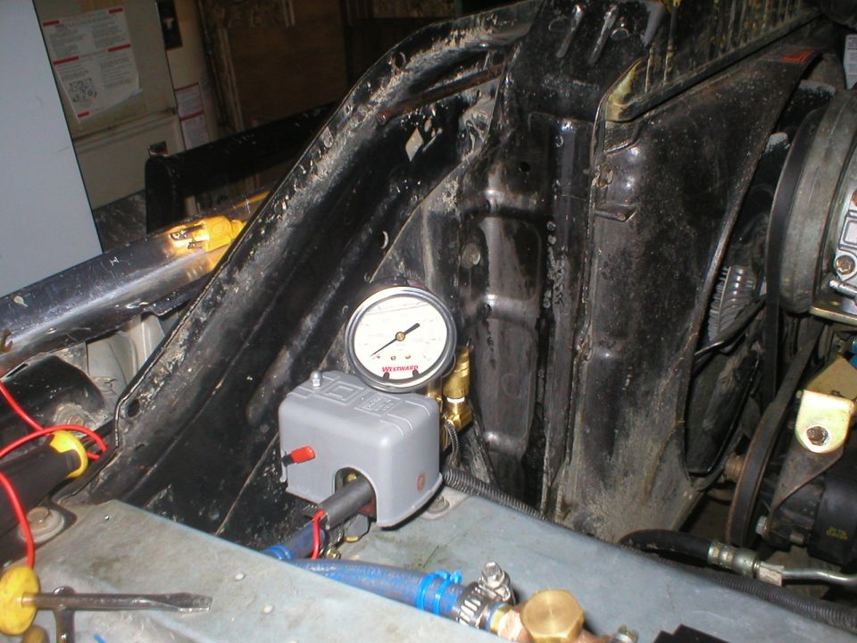 Engine bay with pressure gauge and grey control box, hoses, and wiring visible