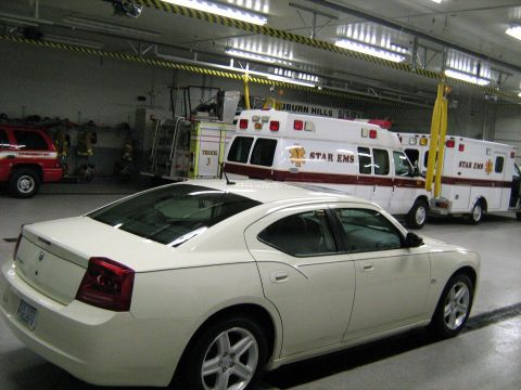 1988 Mercury Grand Marquis - A white sedan is parked inside a fire station, with emergency vehicles visible in the background.