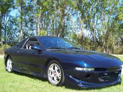 1994 Ford Probe - A dark blue coupe with an aggressive body kit is parked outdoors on a grassy lawn.