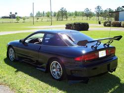 1994 Ford Probe - This dark blue coupe features a prominent rear spoiler, aftermarket wheels, and a custom body kit, suggesting modifications beyond its orig…