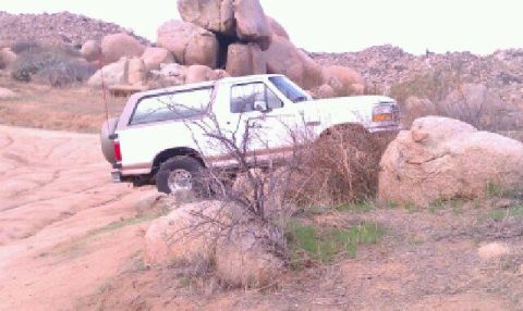 1996 Ford Bronco - A white 1996 Ford Bronco is seen parked on a dirt road surrounded by large rocks and dry brush.