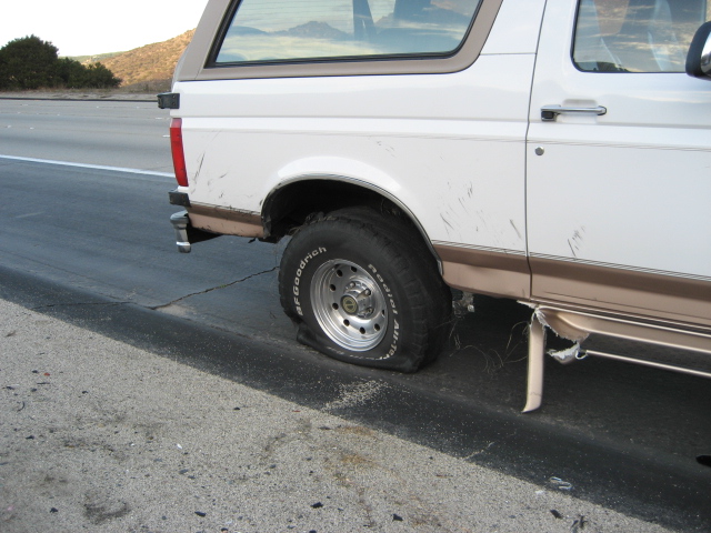 White 1996 Ford Bronco on side of road with flat rear tire