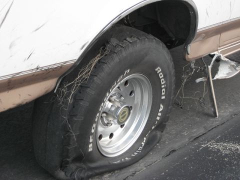 1996 Ford Bronco - A vehicle's flat tire shows damage and debris caught in the tread and wheel well.
