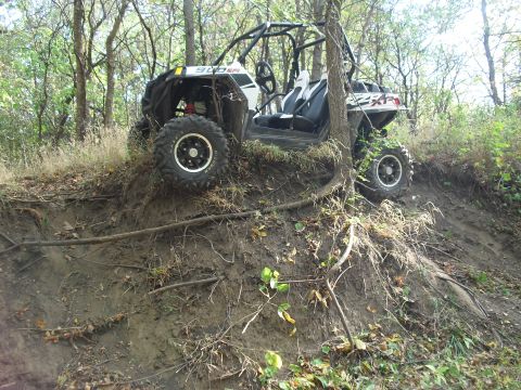1986 Ford Bronco - An off-road vehicle navigates a steep, muddy slope in a wooded area.