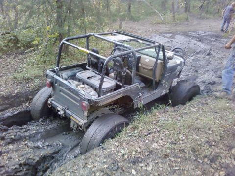 1986 Ford Bronco - Off-road vehicle with roll cage stuck deep in mud, tires submerged.