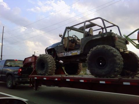 1986 Ford Bronco - A heavily modified Jeep Wrangler with oversized tires is being transported on a flatbed trailer.