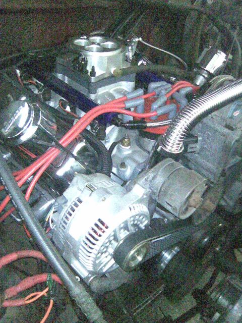 1991 Ford Bronco - Close-up of a V8 engine bay showing a polished aluminum throttle-body/EFI intake, chrome alternator, red spark plug wires, and a braided st…
