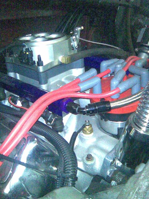 1991 Ford Bronco - Close-up of a V8 engine bay showing a polished aluminum throttle body/fuel injection unit atop the intake, red spark plug wires running to…