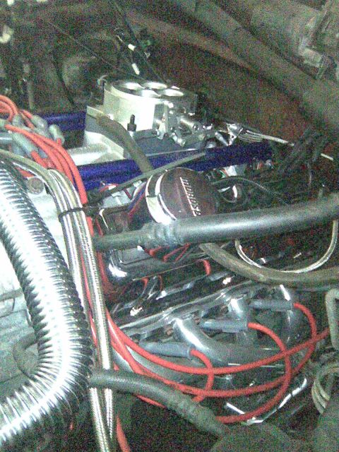 1991 Ford Bronco - Close-up of a modified V8 engine bay showing a polished aluminum throttle-body/intake, a black Edelbrock-style component, red spark plug wi…