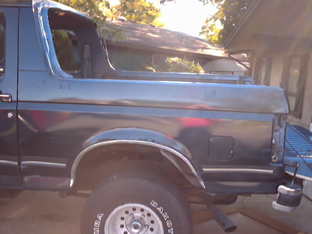 Side view of a dark blue 1990 Ford Bronco with the rear section visible. The tailgate is down