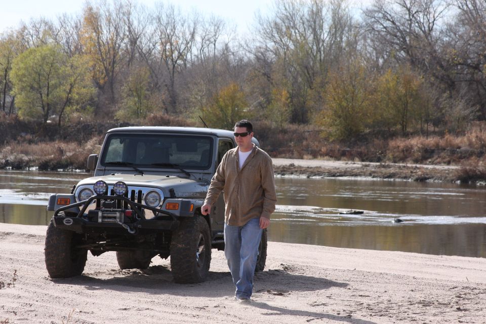 Gray Jeep Wrangler with aftermarket bumper and winch parked on a sandy riverbank