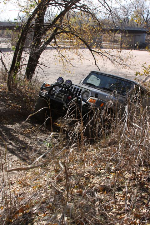 2005 Jeep Wrangler - A Jeep Wrangler navigates a rough, overgrown path near a bridge structure.