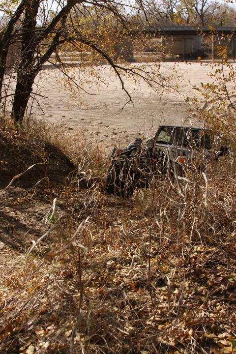 2005 Jeep Wrangler - A dark-colored Jeep Wrangler is partially obscured by dry grass and brush on a dirt embankment, suggesting it is off-road or parked in a na…
