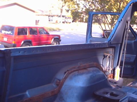 1990 Ford Bronco - View from inside the bed of a blue pickup truck, with a red SUV visible in the background.