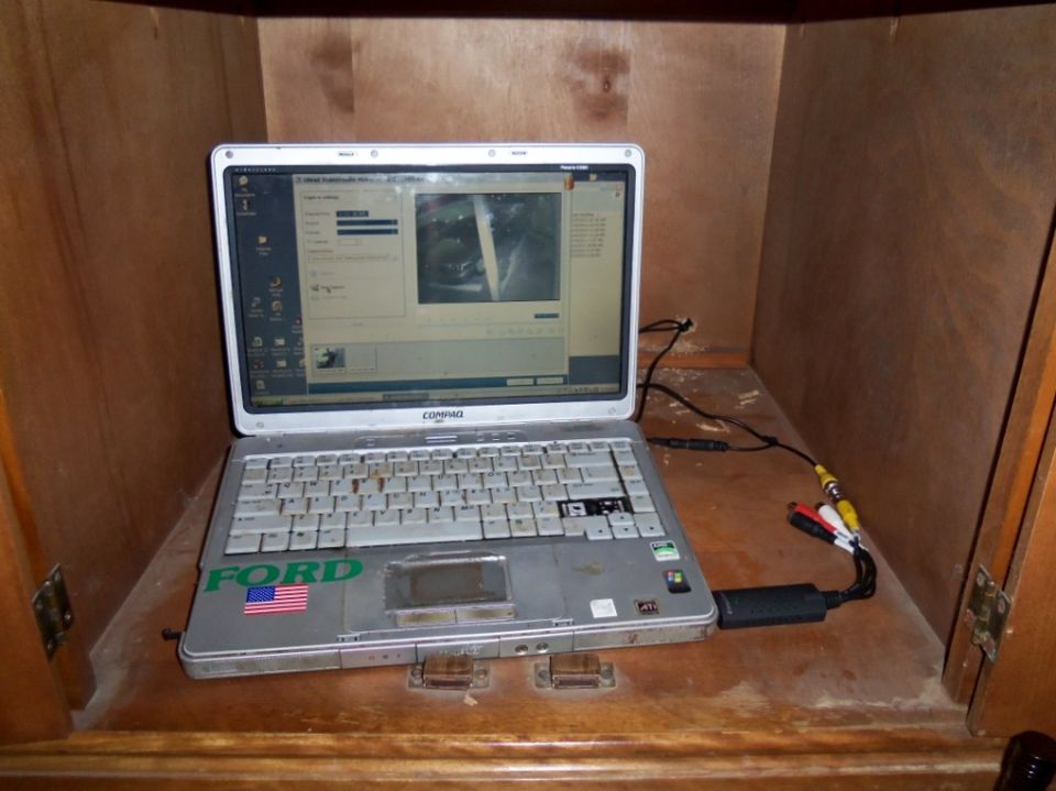 Laptop with a "FORD" sticker and American flag sticker on its lid, connected to a video capture device