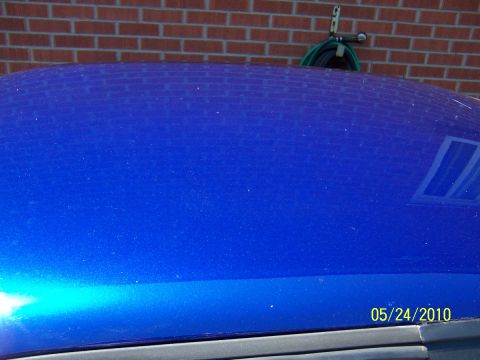 1993 Ford Probe - A blue car's roof is visible, with a brick wall and hose reel reflected on its surface.