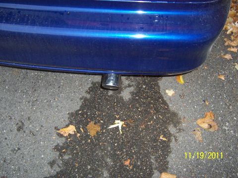 1993 Ford Probe - Close-up of a car's rear bumper and exhaust pipe, with a water puddle on the ground.