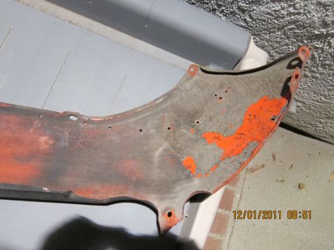 1969 Ford Mustang - This is a part of a car fender, painted orange, with several mounting holes visible.