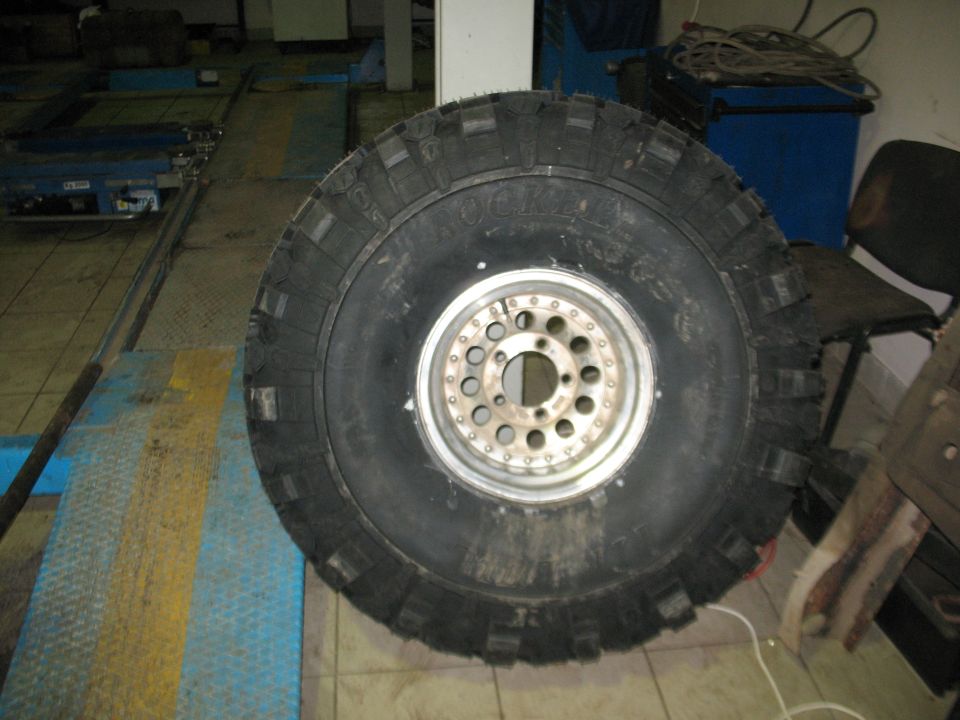 Large mud-terrain tire on a chrome beadlock-style wheel standing in a shop