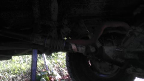 1989 Ford Bronco - A view of the underside of a vehicle, focusing on suspension parts and a tire, with a jack stand visible.