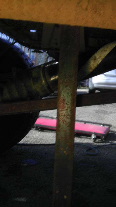 1989 Ford Bronco - Close-up of the undercarriage, showing mechanical parts and a glimpse of the surroundings.