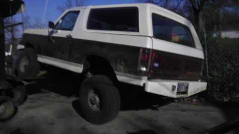 1989 Ford Bronco - A lifted, two-tone Ford Bronco is parked outdoors, showing its rear end and suspension.