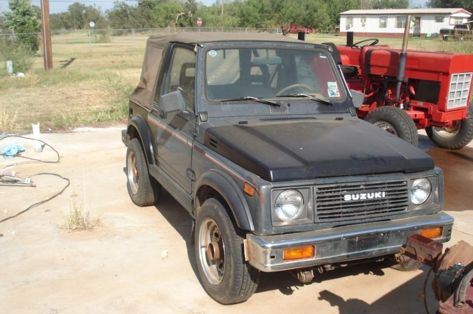 Gray Suzuki Samurai parked next to a red tractor