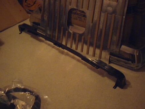 1990 Ford Bronco - A black car bumper part is shown on a carpeted surface, with a metal grille visible behind it.
