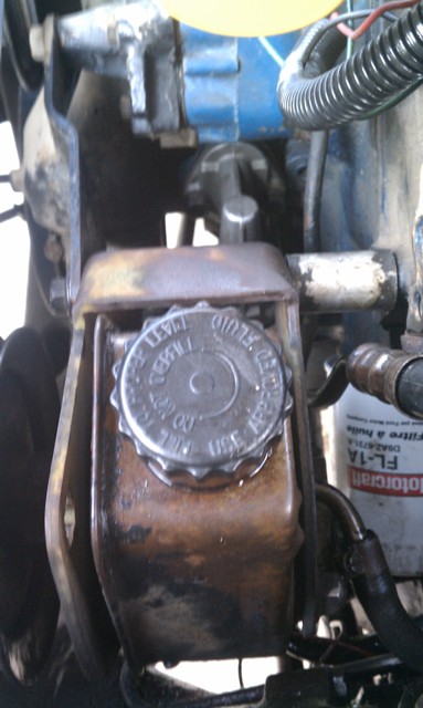1978 Ford Bronco - Close-up of a power steering fluid reservoir with a metal cap indicating fluid level instructions.