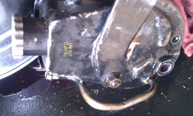 Close-up of a black power steering pump with some yellow text and a metal loop