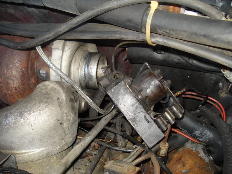 Engine bay with turbocharger, hoses, and electrical connectors. Rusty metal visible