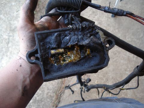 1989 Ford F-250 - A severely damaged electrical part, likely from an engine bay, shows melted plastic and a burnt capacitor.