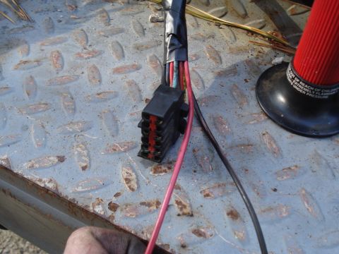 1989 Ford F-250 - A wiring harness connector with exposed wires is shown on a metal surface, with a red object and text in the background.