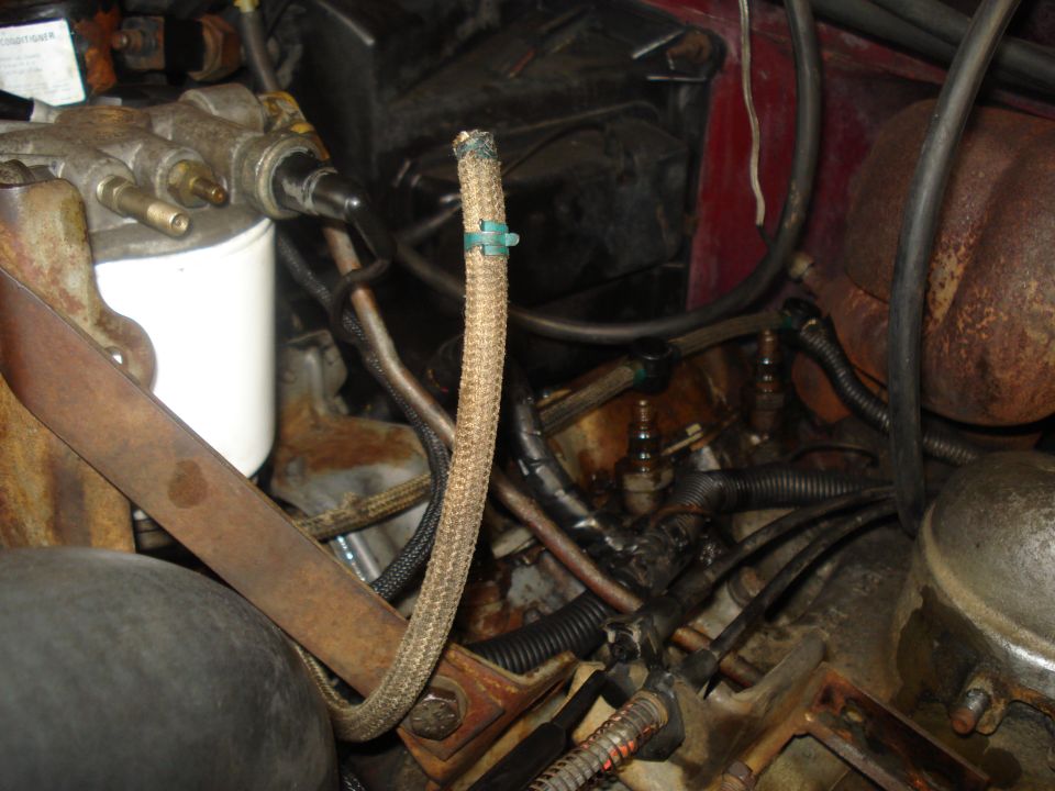 Engine bay showing a white fuel filter, braided hose with a green clip, and various wires and metal components