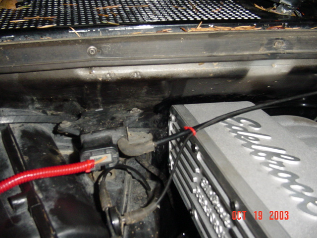 Close-up of engine bay corner showing red battery cable and an Edelbrock component, Oct 2003