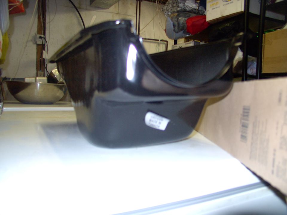 Black plastic engine oil pan on a white workbench in a cluttered garage